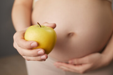 Unknown pregnant woman holding organic yellow apple enjoying healthy nutrition during pregnancy unrecognizable expectant lady having vitamin snack at home