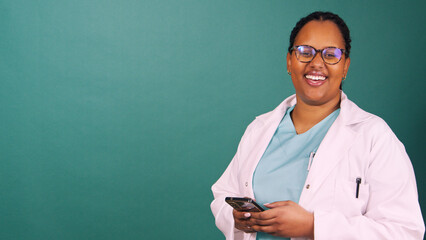 Young Black female doctor works on cellphone, smiles at the camera, copy space