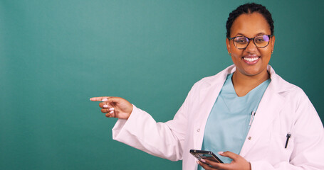Young Black female doctor works on cellphone, smiles at the camera, pointing