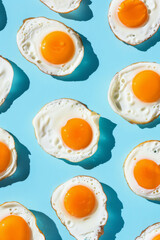 A pattern of fried eggs on a bright pastel blue background, minimalistic food photography. Breakfast concept.