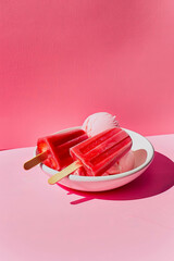 A strawberry popsicle on top of an ice cream dish, with a pink background. Minimalist photography style. Summer food.