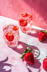 Pink aesthetic background, a pink shadow on the wall, pink strawberry cocktail and water in glasses. Summer drinks.