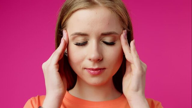 Young Woman Experiencing a Headache Against a Pink Background