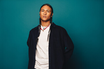 Confident native american man with stylish braided hair and jewelry standing on blue background