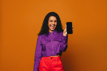 Cheerful woman smiling and recommending smartphone app on vibrant orange background - obrazy, fototapety, plakaty