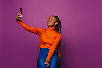 Smiling african woman taking a selfie with smartphone on a vibrant purple background - 773852574