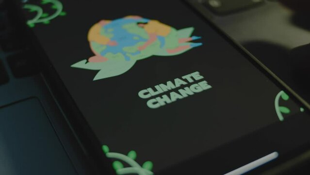 Climate change inscription on black background on smartphone screen. Drawn image of humans hugging Planet Earth. Environment concept. Male hand flapping fingers cheerfully