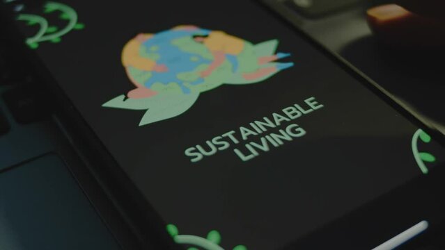 Sustainable living inscription on black background on smartphone screen. Drawn image of two humans hugging Planet Earth. Environment concept. Male hand flapping fingers cheerfully