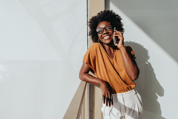 Happy business woman chatting on the phone in a sunny modern workspace