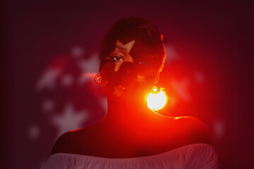 Confident African, attractive woman with a star symbol on her face in red light. Authentic and...