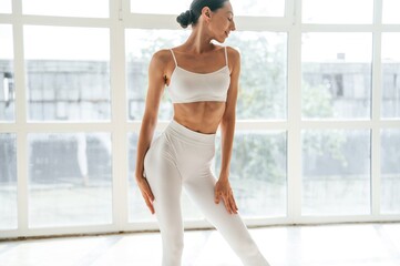 Natural lighting. Woman in fitness clothes is standing against window with view
