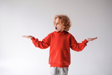 A cheerful red-haired boy in a red T-shirt gestures with his hands, A place for advertising on a gray background