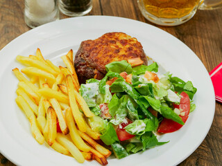 Burger with melted cheese toping, fresh green salad with lettuce and tomato and cucumber and fired potato chips on a wooden table. Tasty dinner. High quality product meal. Close up.