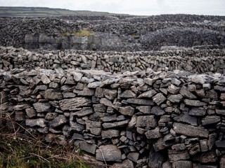 Traditional dry stone fence by a field. Aran islands, county Galway, Ireland. Popular tourist area with stunning nature scenery and endless stone fences. Old craft and simple construction material.