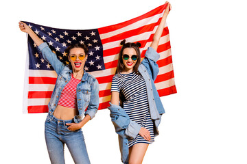Two adorable good-looking travel trip lady in casual denim jeans trendy glasses spectacles isolated on yellow vivid background raised usa flag make beaming grinning friendly optimist hollywood smile - obrazy, fototapety, plakaty