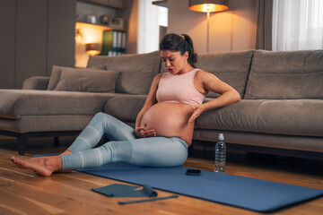 An active pregnant woman having contractions and taking a break from her home workout