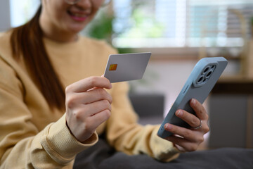 Cropped shot smiling young woman holding credit card and smartphone at home