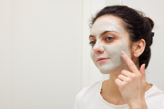 Caucasian woman looking in mirror and applying face mask white in bathroom. copy space