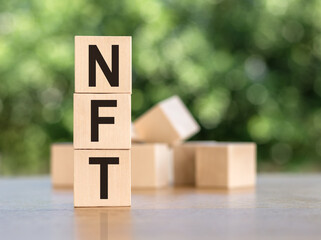 the word NFT is laid out of wooden cubes with letters on green background. NFT - non fungible token - is a special crypto token that uses blockchain technology to link with a digital asset