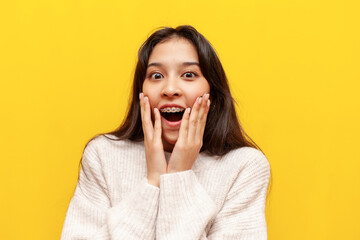 young shocked asian girl with braces wonders on yellow isolated background, amazed korean girl...