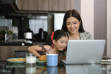 Beautiful single mother working on laptop at home with daughter. Motherhood and child care concept