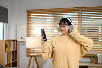 Cheerful asian woman wearing headphones and singing her favorite song at home