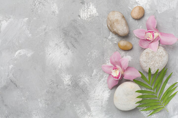 Fototapeta na wymiar Composition with orchids and massage stones on concrete background, top view