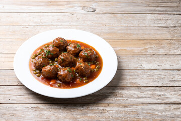 Meatballs, green peas and carrot with tomato sauce on wooden table. Copy space