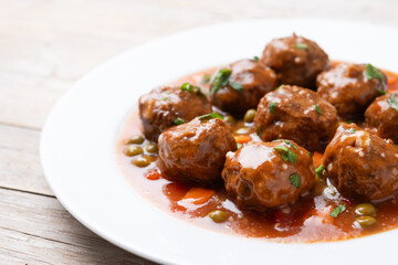 Meatballs, green peas and carrot with tomato sauce on wooden table