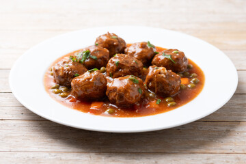 Meatballs, green peas and carrot with tomato sauce on wooden table