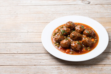 Meatballs, green peas and carrot with tomato sauce on wooden table. Copy space