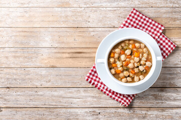 Chickpeas soup with vegetables in bowl on wooden table. Top view. Copy space