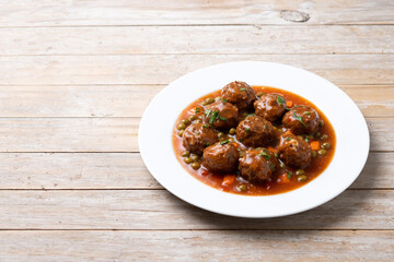 Meatballs, green peas and carrot with tomato sauce on wooden table. Copy space