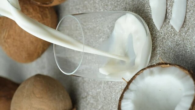 Coconut milk pouring into a glass among coconuts, vertical slow motion.