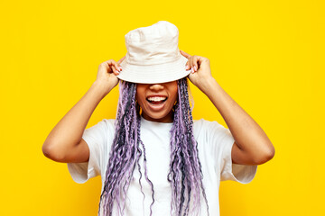 young african american woman with hipster colored dreadlocks wears panama hat on yellow isolated...