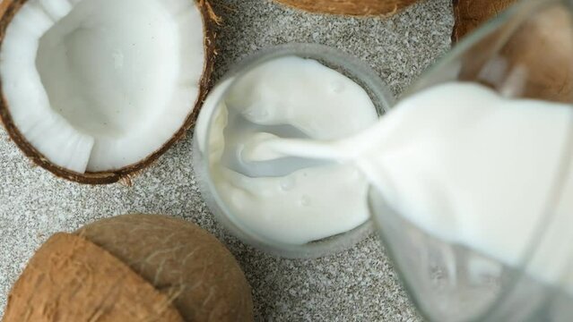 Coconut milk pouring into a glass among coconuts, top view, slow motion.