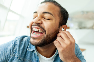 happy african american man with braces listens to music and laughs in a white cafe, the man holds a...