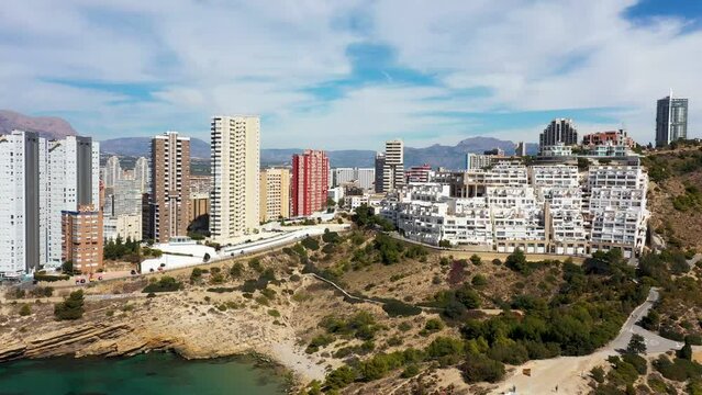 Aerial drone footage or the north part of Benidorm in Spain showing the rocky paths by the ocean in the summer time and the beach known as The Cala Tio Ximo Beach