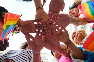 A group of multiracial people with rainbow LGBTQ bracelets stacking hands. Scene is one of unity...