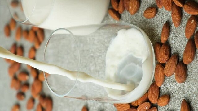 Almond milk pouring in a glass on grey background, vertical slow motion.