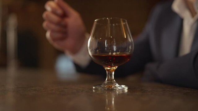 Close-up of a man in a suit puts a glass of cognac on the bar. Nightlife, relaxation