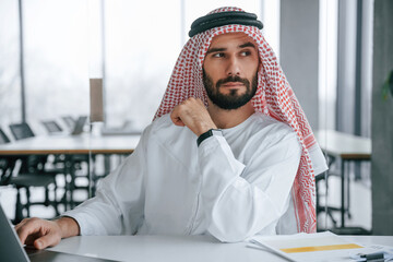 Normal work day. Successful Muslim businessman in traditional outfit in his office