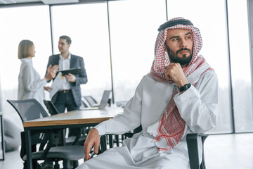 Serious facial expression. Muslim businessman in traditional outfit with colleagues in office