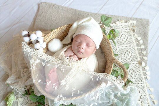 A Taiwanese newborn baby wrapped in a white wrap is taking a newborn photography while sleeping. 白いおくるみを巻いた台湾人の新生児の赤ちゃんが寝ている間にニューボーンフォトを撮影されている 