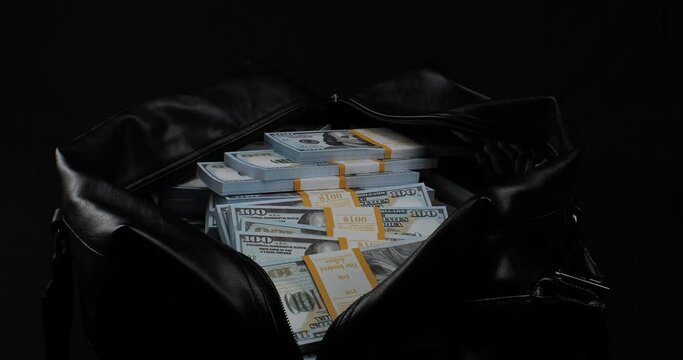 On a black background, I put stacks of hundred dollar bills into a large bag. A man in business clothes puts stacks of dollars in a bag. Accumulated money in large bags on a black background.