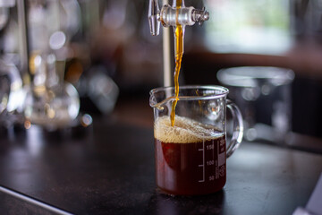 Selective focus, clear measuring cup for brown drip coffee. A clear measuring glass like those used in science laboratories. In a premium coffee shop in Thailand