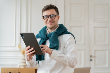 A delighted man with a keen look on his face comfortably handles a tablet, his attire suggesting a...