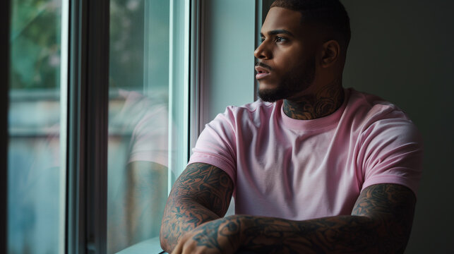 the stillness of the room, a man in a pink t-shirt leans against a window frame, his arms a canvas of intricate tattoos that reflect his innermost thoughts and experiences