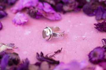 Silver ring with pink stone on a pink background with dry purple flowers. Handcraft precious item....