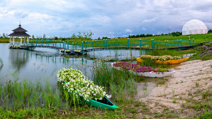 Flowered Wharf: Boat, Bridge, and Gazebo on Riverbank - 773934759